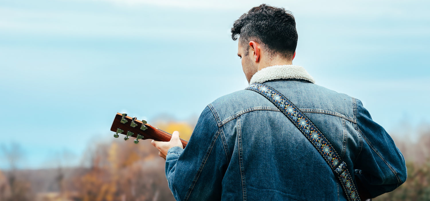 Jeremie Legault, the pop-rock sensation, exudes charisma in a denim jacket with a wool neckline, playing an acoustic Martin guitar in a picturesque rural setting. 